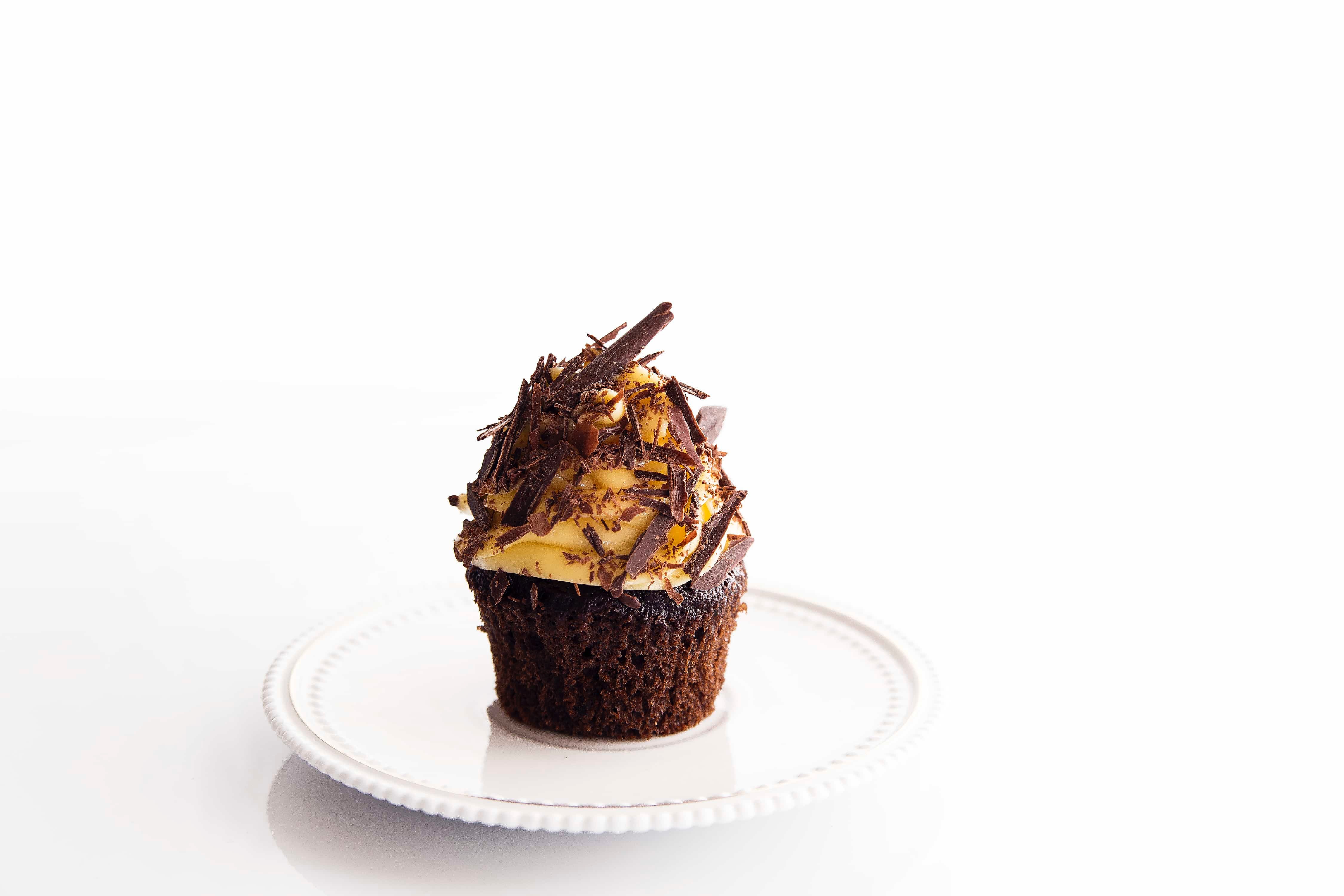 Chocolate cupcake with caramel buttercream and Chocolate Shavings, on round white ceramic plate